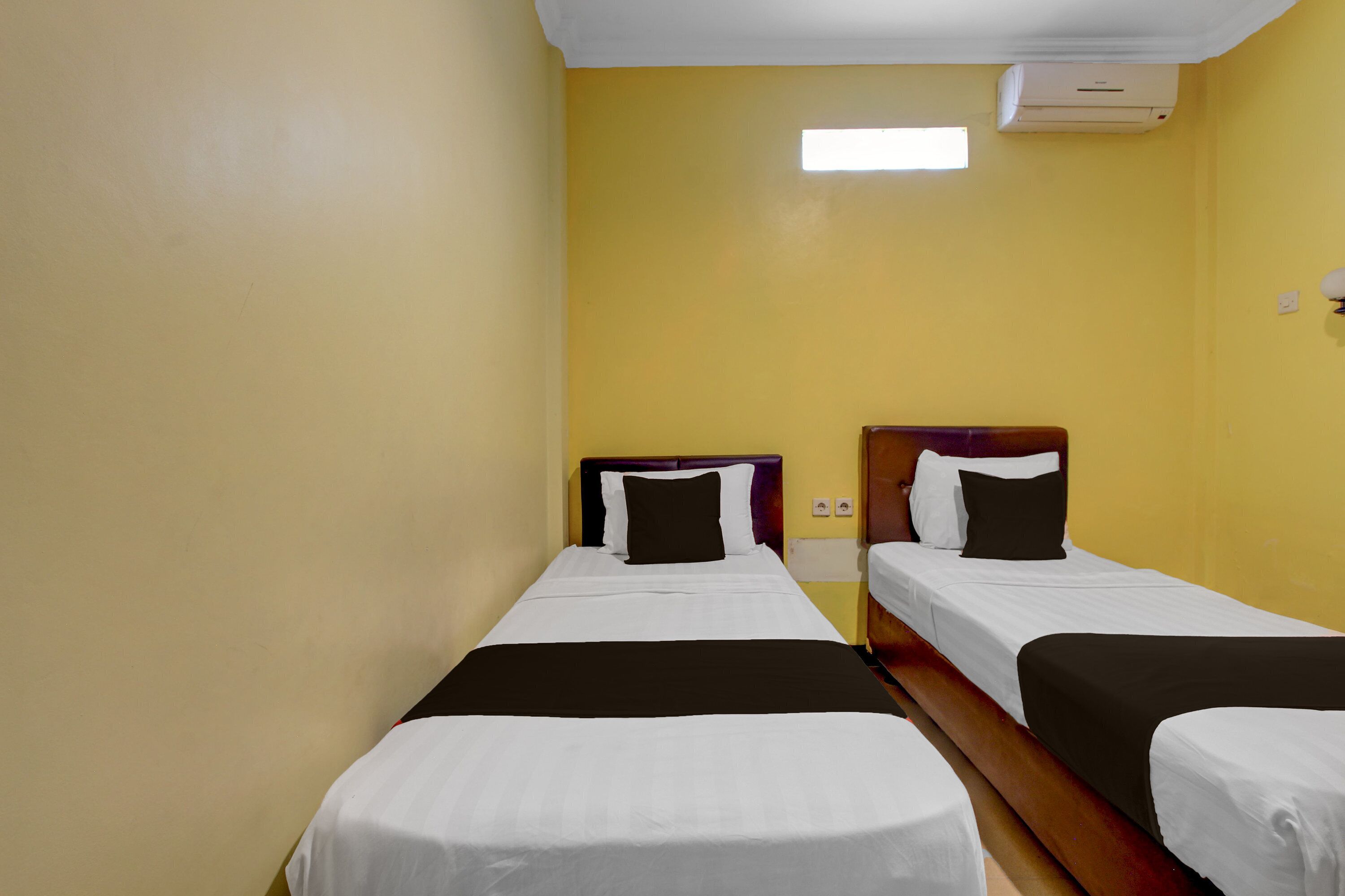 Una habitación de hotel con dos camas individuales, un cabecero de madera y un ventanal pequeño.