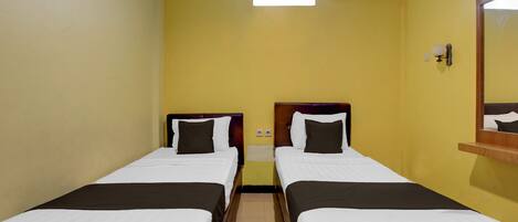 A hotel room with two single beds, a small window, an air conditioning unit, and a mirror on the wall.