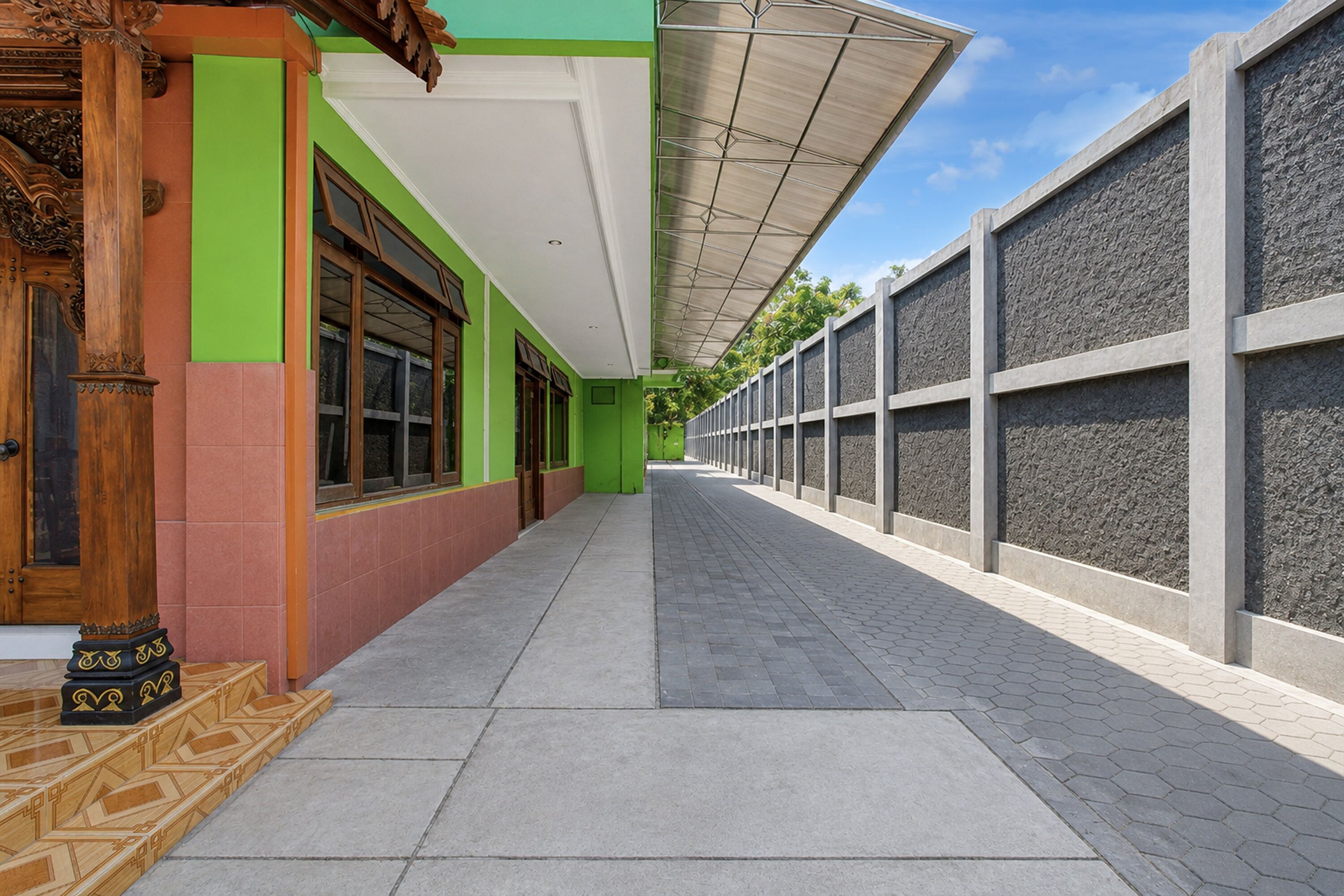 A covered walkway with a tiled floor, green and red walls, and a stone wall on the right.