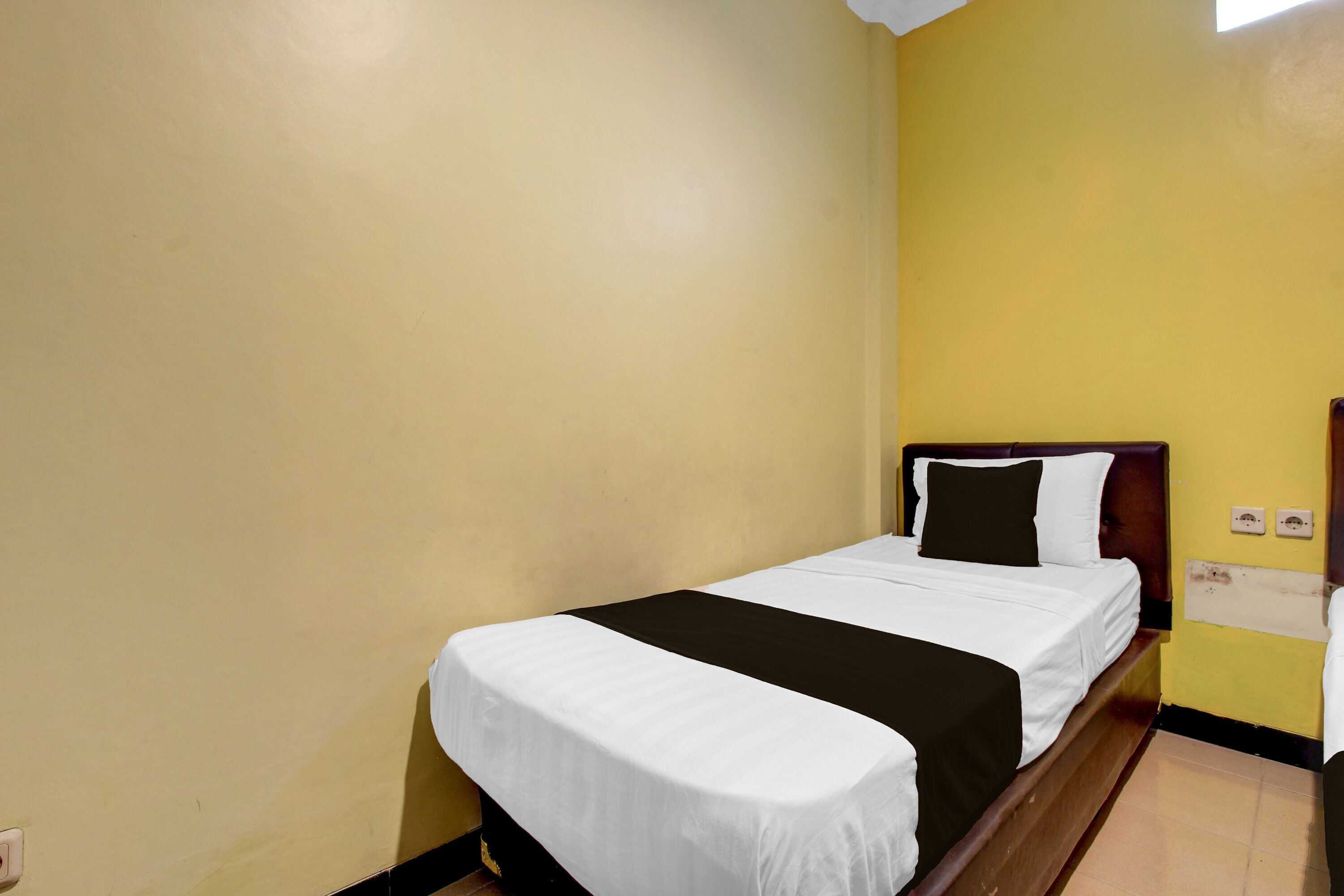 Uma cama de solteiro com colcha preta e branca num quarto com paredes amarelas.