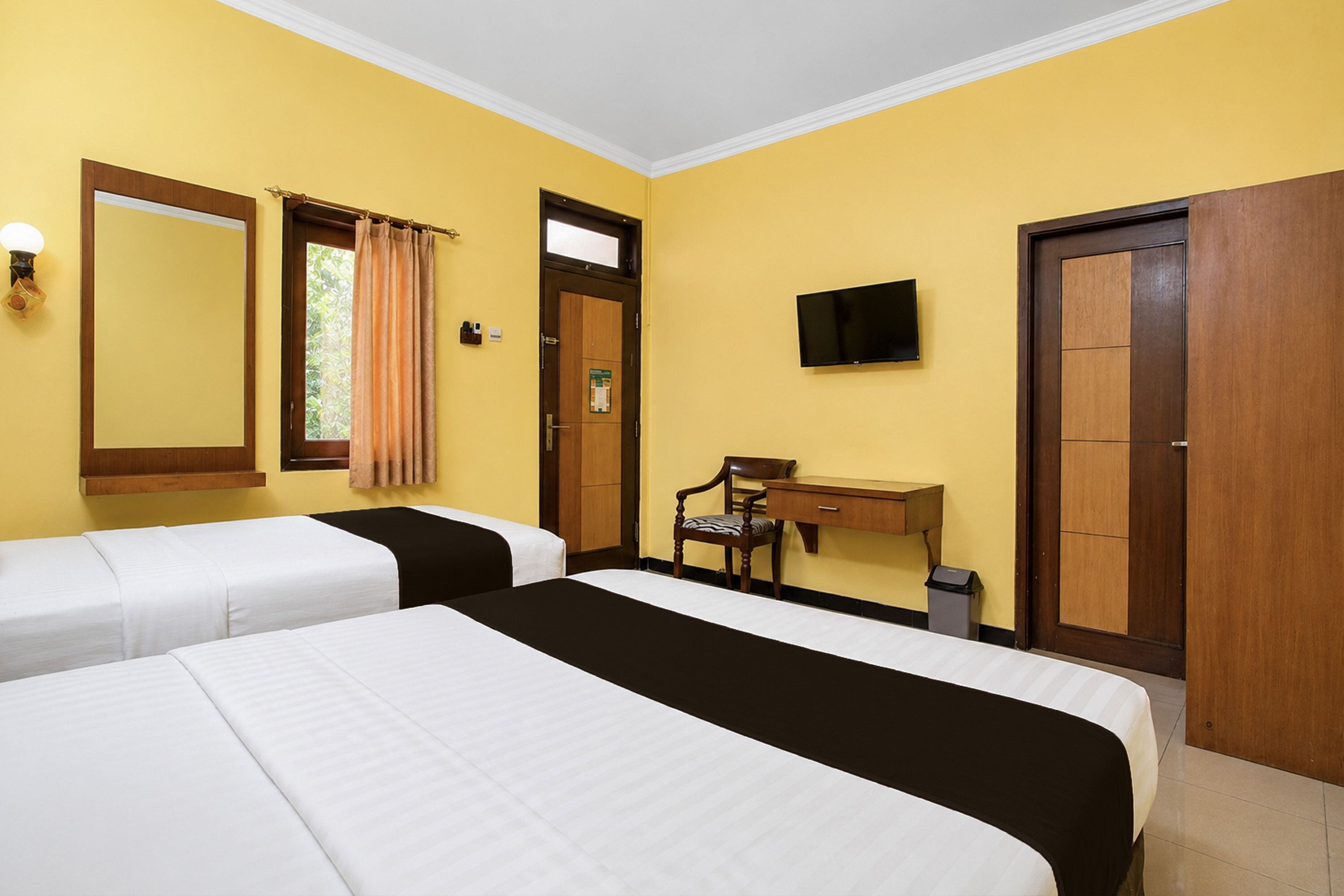 Habitación de hotel con dos camas, un escritorio, una silla, un televisor y una puerta.