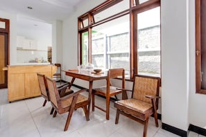 Zona pranzo con tavolo e sedie in legno, cucina sullo sfondo e ampie finestre con vista su un muro di pietra.