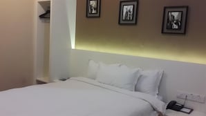 A hotel room with a bed, white bedding, a bedside telephone, and three framed pictures on the wall.
