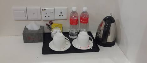 A hotel room's breakfast setup with a coffee maker, two cups, two bottles of water, a tissue box, and a packet of tea.
