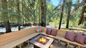 Un patio in legno con un braciere e un'area salotto, circondato da alberi.