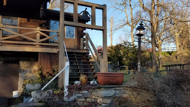 A rustic wooden staircase leading to a wooden deck with a bell and lantern. - Log cabin nestled beside Chiques Creek in historic Lancaster County (Mount Joy)