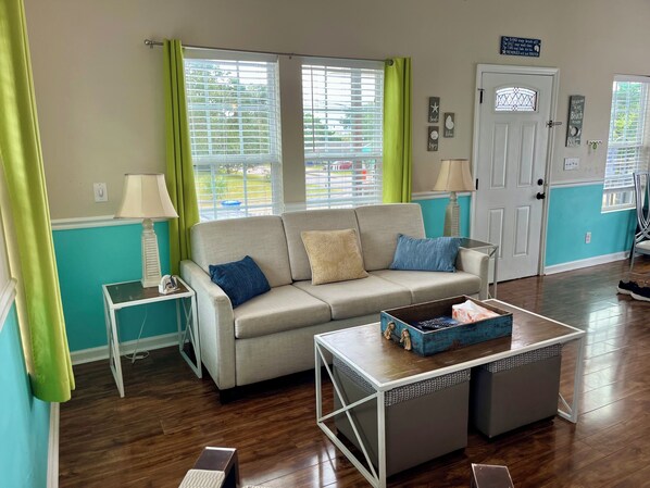 Una sala de estar con un sofá color beige, dos mesas auxiliares, una mesa de centro y una puerta.