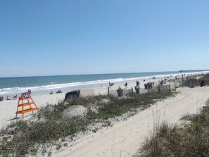 Una playa con una valla de madera, una torre de salvavidas y un muelle a lo lejos.