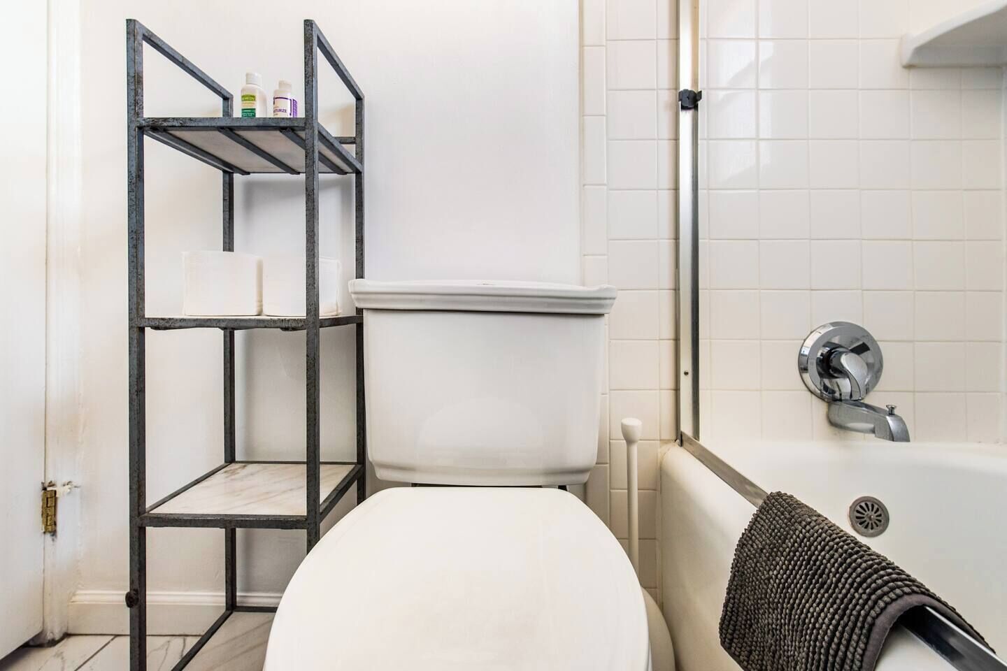 Kylpyhuone, jossa on wc, kylpyamme ja metallinen hyllykkö.