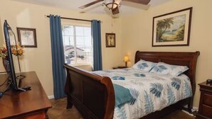 Un dormitorio con una cama de madera, un ventilador de techo, un escritorio con una computadora y una ventana con cortinas.