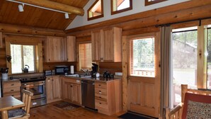 Cocina tipo cabaña con gabinetes de madera, estufa, microondas, lavamanos y comedor con mesa y sillas de madera.