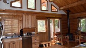 Interior de una cabaña de madera con cocina, comedor y chimenea.
