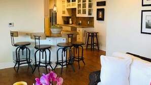 A living room with a sofa, a coffee table, and a dining area with chairs and a kitchen in the background. - LUX Beachfront Casa de Balboa 231 w/AC - Best View (Newport Beach)