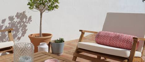 A wooden outdoor seating area with a white cushioned chair and a small potted plant.