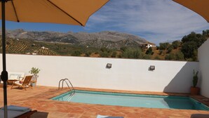 A swimming pool with a view of mountains, a white wall, and a patio area with lounge chairs and a potted plant. - Rural villa in Marrucho Alto (Riogordo)