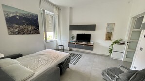 Ein modernes Schlafzimmer mit Bett, Fernseher, kleinem Tisch und Stuhl.