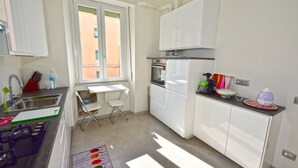 Eine moderne Küche mit weißen Schränken, einem Gasherd, einem kleinen Esstisch und einem Fenster mit Blick ins Freie.