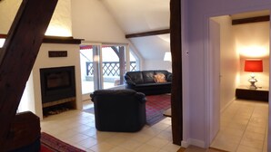 Un salon aménagé dans les combles, avec une cheminée, un canapé en cuir noir et un tapis rouge.