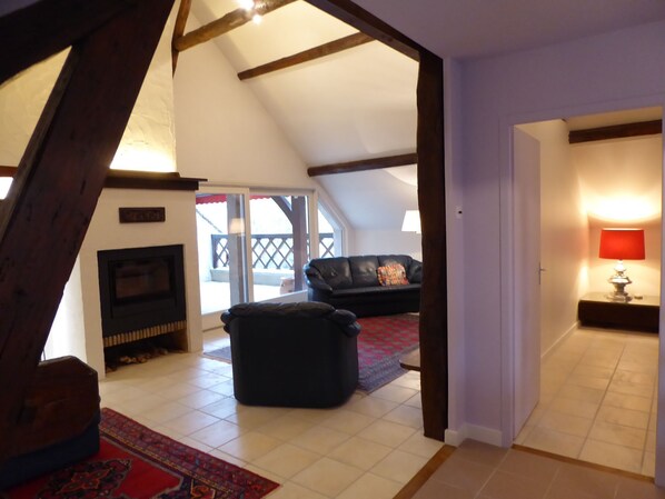 Un salon aménagé dans les combles, avec une cheminée, un canapé en cuir noir et un tapis rouge.