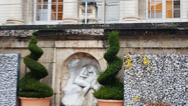 Un bâtiment à l’architecture classique, une statue et des plantes en pot.