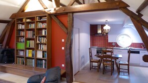 Un espace de vie de style « loft », avec des poutres en bois apparentes, une bibliothèque, un coin repas et une cuisine aux carreaux rouges.