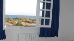 A bedroom with a bed, a window with curtains, and a view of the outdoors. - Apartment with sea view (Hammamet)
