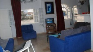 A living room with a blue sofa, a television, and a chandelier. - Apartment with sea view (Hammamet)