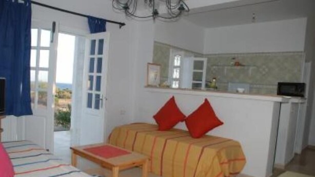 A room with a bed, a small table, a kitchenette, and a view through a door. - Apartment with sea view (Hammamet)