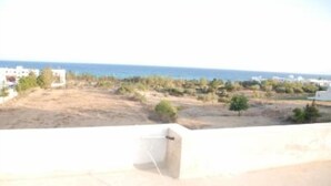 A view from a balcony overlooking a coastal area with buildings and trees. - Apartment with sea view (Hammamet)