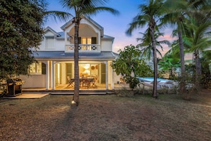 A two-story house with a balcony, a patio with outdoor furniture, and a swimming pool.
