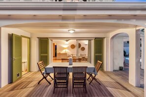 A covered outdoor dining area with a table and chairs, a lamp, and a view of the interior.