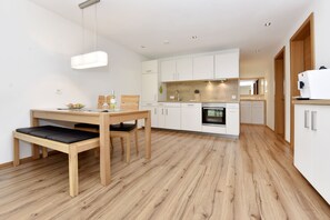 Een moderne keuken met witte kasten, een houten eettafel met een bank, en een inbouwoven.