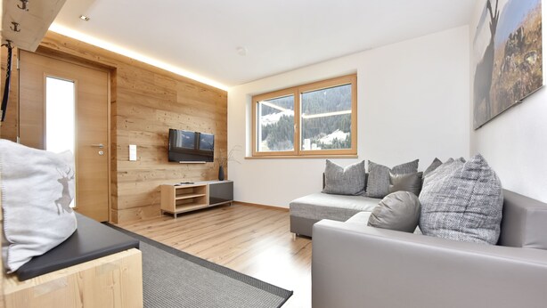 Una sala moderna con una pared de madera, un sofá gris y un televisor.