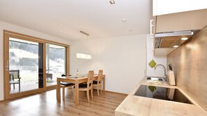 Una cocina moderna con una mesa y sillas de madera, estufa empotrada y un gran ventanal corredero que da a un espacio exterior nevado.