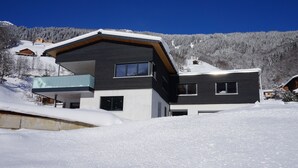 Una casa moderna de dos pisos con balcón, rodeada de colinas nevadas.