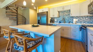 A modern kitchen with a central island, white cabinetry, a stainless steel refrigerator, and a blue-tiled backsplash. - Remodeled!! Koa Resort #5J 2-Bd 2-Ba, A/C, South Maui, Walk To 3 Beaches! (Kihei)