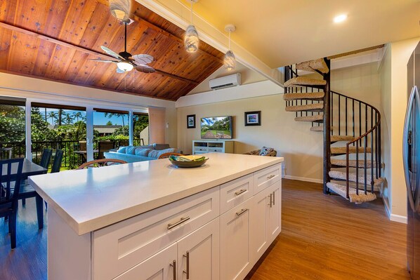 A modern kitchen with a wooden ceiling, a white island, and a spiral staircase.
