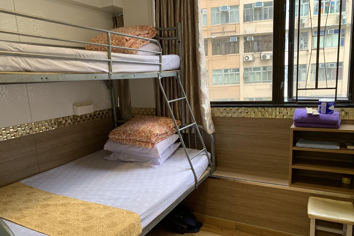 A bunk bed room with a wooden floor, a desk with a chair, and a window with curtains.