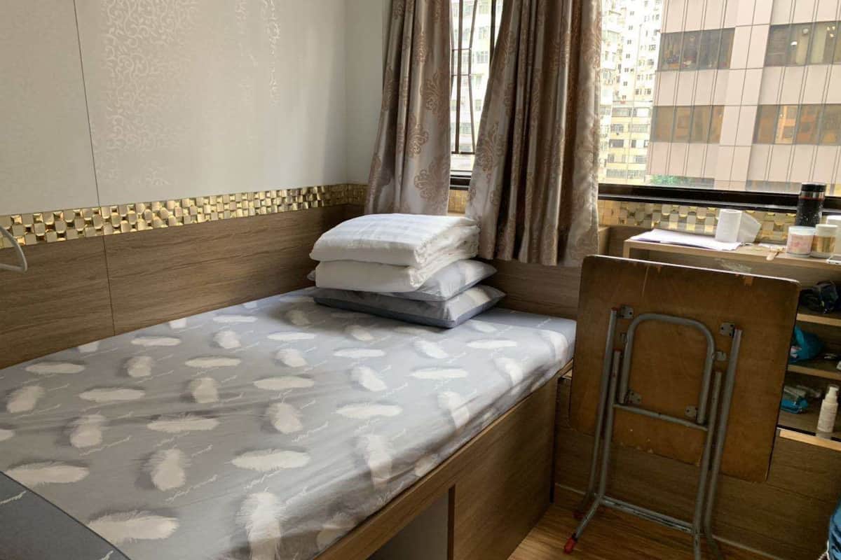 A compact room with a bed, a small desk, and a window with curtains.