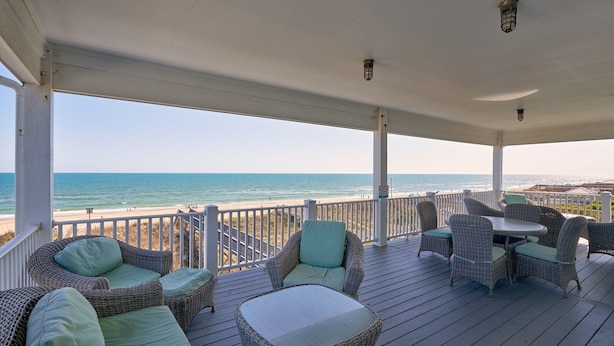 A covered deck with wicker furniture and a view of the ocean.