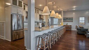 A modern kitchen with stainless steel appliances, a long bar counter with stools, and pendant lighting.
