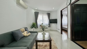 A modern living room with a sofa, a coffee table, a TV, and a window with curtains. - Sabay Airport Apartment (Ho Chi Minh City)