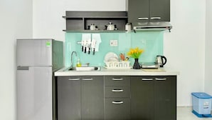 A compact kitchen with a built-in refrigerator, a sink, and a stove. There are cabinets with handles, a dish rack, and a trash bin. - Sabay Airport Apartment (Ho Chi Minh City)