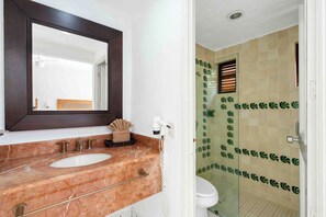 A bathroom with a marble sink, a mirror, and a shower with patterned tiles.