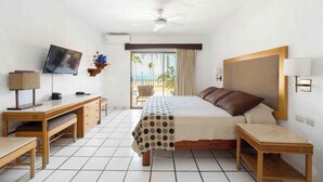 Ein Hotelzimmer mit Bett, Schreibtisch, Fernseher und einem Balkon mit Blick auf Palmen.