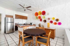 A modern kitchen with a dining area, featuring a round table, wooden chairs, a refrigerator, and a ceiling fan.