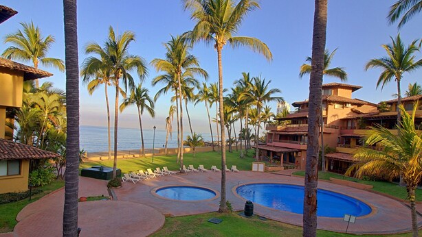 Ein Resort mit Poolbereich, Palmen und Blick auf den Ozean.