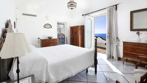 Een slaapkamer met een bed, een dressoir en uitzicht op zee.