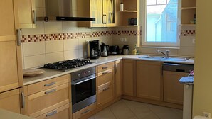 Een keuken met houten kastjes, een gasfornuis, een oven, een koffiezetapparaat en een raam met uitzicht.