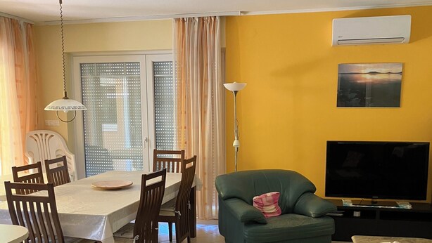 Een woonkamer met een eethoek, een groene bank, een televisie en een plafondventilator.
